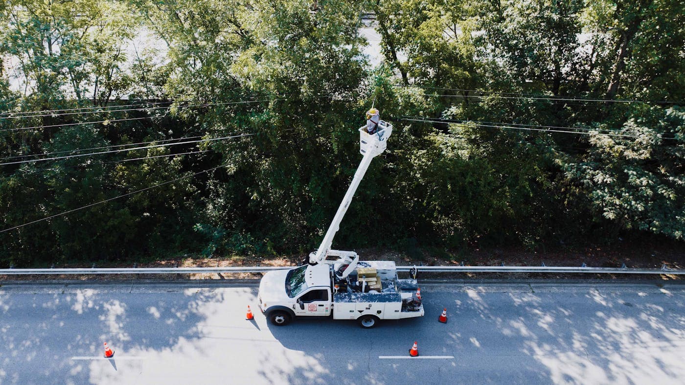 Aerial view of a tree service bucket truck working along a tree-lined road